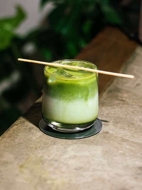 An iced matcha latte in a glass with a bamboo scoop